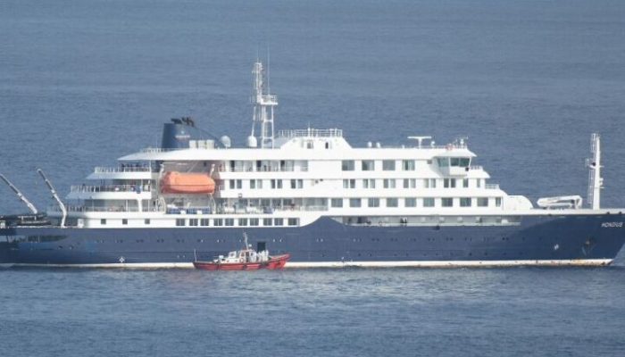 An ambulance boat carrying crew members wearing hazmat suits, approaches the pilot door on the starboard side of the cruise ship MV Hondius, while stationary off the port of Praia, the capital of Cape Verde, on May 5, 2026 as passengers look on from the bridges. Two seriously ill crew members on a cruise ship stricken by a deadly hantavirus outbreak will be evacuated via Cape Verde to the Netherlands, allowing the vessel to sail on to Spain's Canary Islands, the ship operator said Tuesday.
The MV Hondius has been at the centre of an international health scare since Saturday, when WHO was informed that the rare disease -- usually spread from infected rodents typically through urine, droppings and saliva -- was suspected of being behind the deaths of three of its passengers.
As others fell ill, passengers and crew have been in isolation after Cape Verde authorities barred the ship from docking, and as health authorities scrambled to find a port that would take the Hondius. (Photo by AFP)